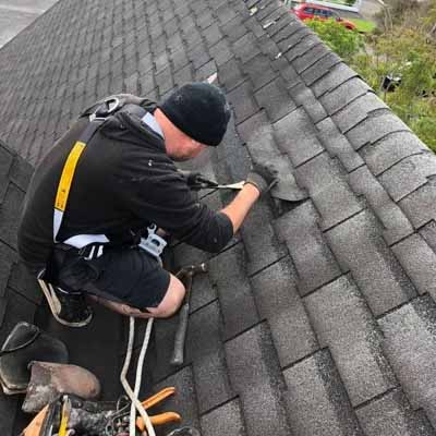 Roofer repairing and inspecting grey asphalt shingles on a residential roof in New Zealand