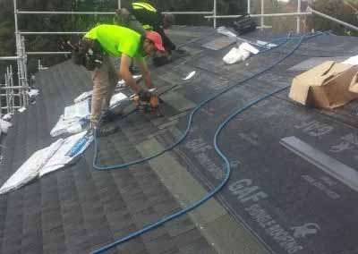 Roofers installing dark asphalt shingles on a New Zealand residential roof during re-roofing work